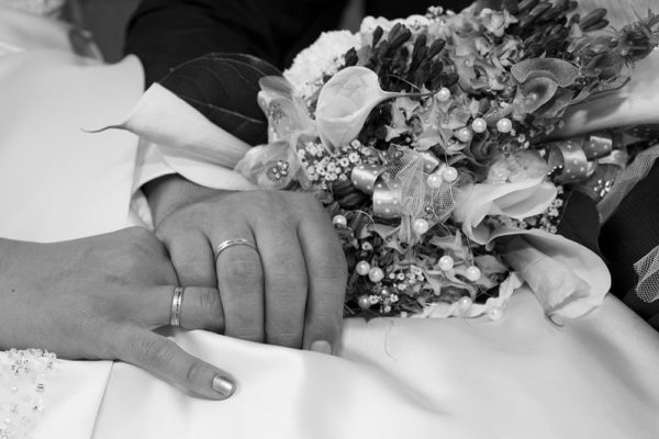 Ein Mann hält zärtlich nach der Hochzeit die Hand seiner Braut. Man sieht die Ringe und den Blumenstrauß. Foto wurde gemacht von Wilhelm Watschka