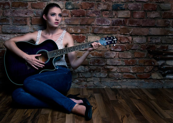 Foto: Wilhelm Watschka Fotografie I Eine Frau sitzt in einem Raum am Boden und spielt Gitarre.