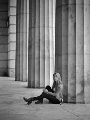 Fotograf: Wilhelm Watschka Fotografie I Eine Frau sitzt bei Säulen auf dem Boden und winkelt ein Bein an.